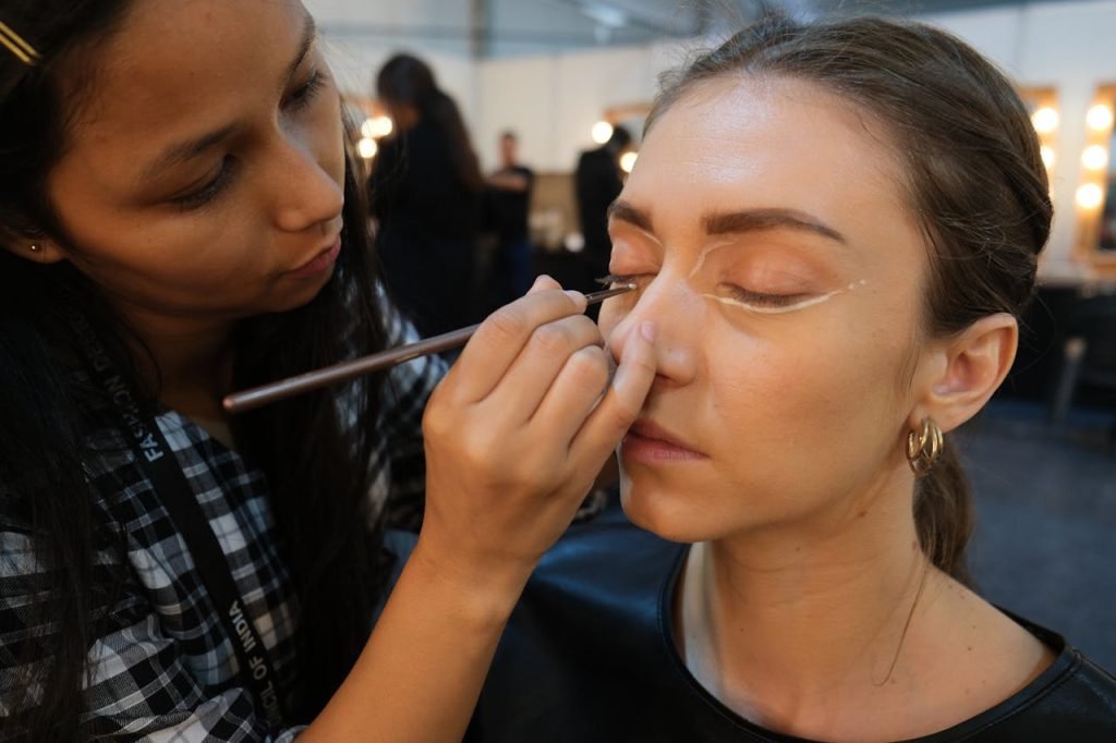 two-woman-3089849 A makeup artist skillfully applies eye makeup to a model during a professional photoshoot.