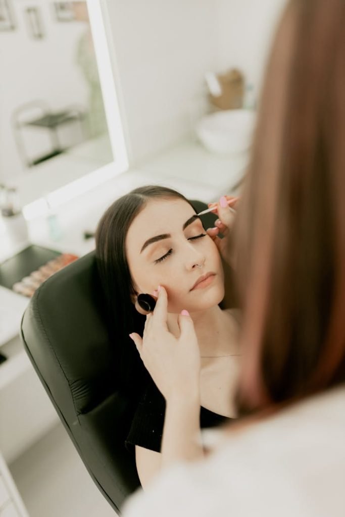 woman-receives-professional-makeup-application-29588093 Makeup artist applying eyeliner to a woman in a beauty salon setting.
